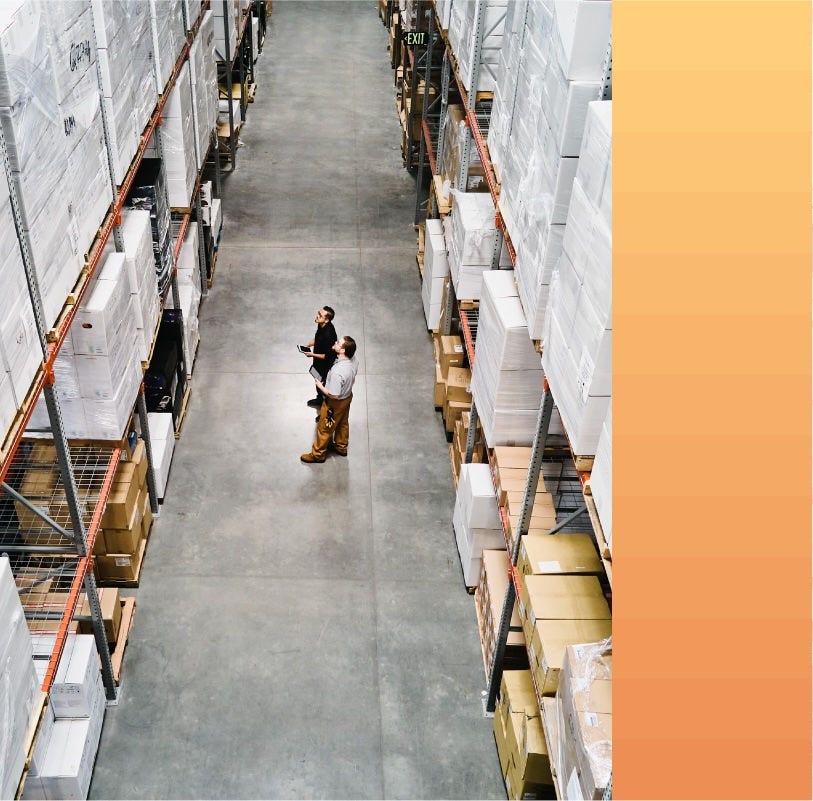 Warehouse employees examine boxed products in a wide aisle.